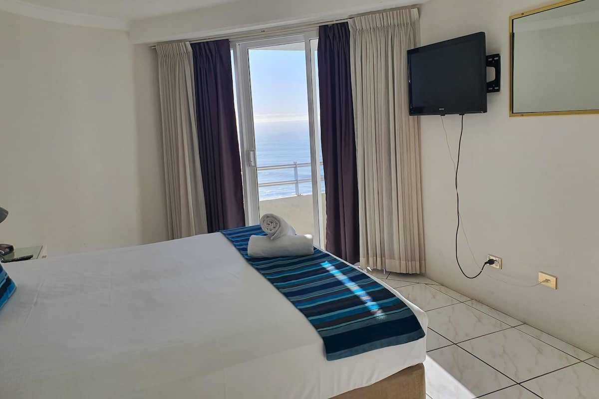 Une chambre d’hôtel avec un lit, un téléviseur fixé au mur et une vue sur la mer par la fenêtre.