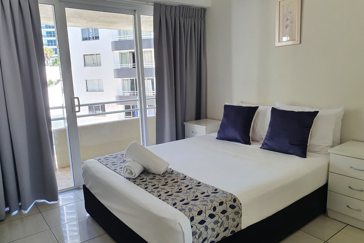 Une chambre d’hôtel avec un lit, une table de chevet, un tiroir, une fenêtre avec des rideaux et une vue sur un bâtiment à l’extérieur.