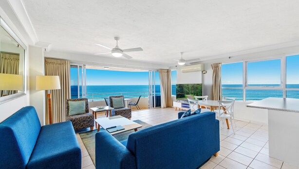 Una habitación de hotel moderna con balcón, un sofá, una mesa de comedor y vista al mar.