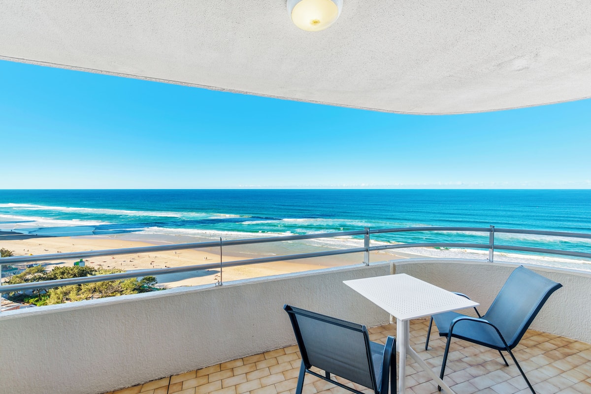 Un balcon avec une table et des chaises donnant sur une plage et l’océan.