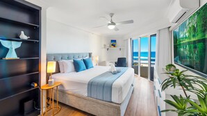 Una habitación de hotel moderna con una cama grande, ventilador de techo, escritorio y vista al océano.