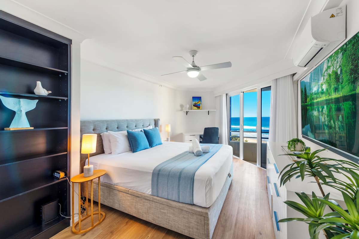 Une chambre d’hôtel moderne dotée d’un grand lit, d’un ventilateur de plafond, d’un bureau et offrant une vue sur l’océan.