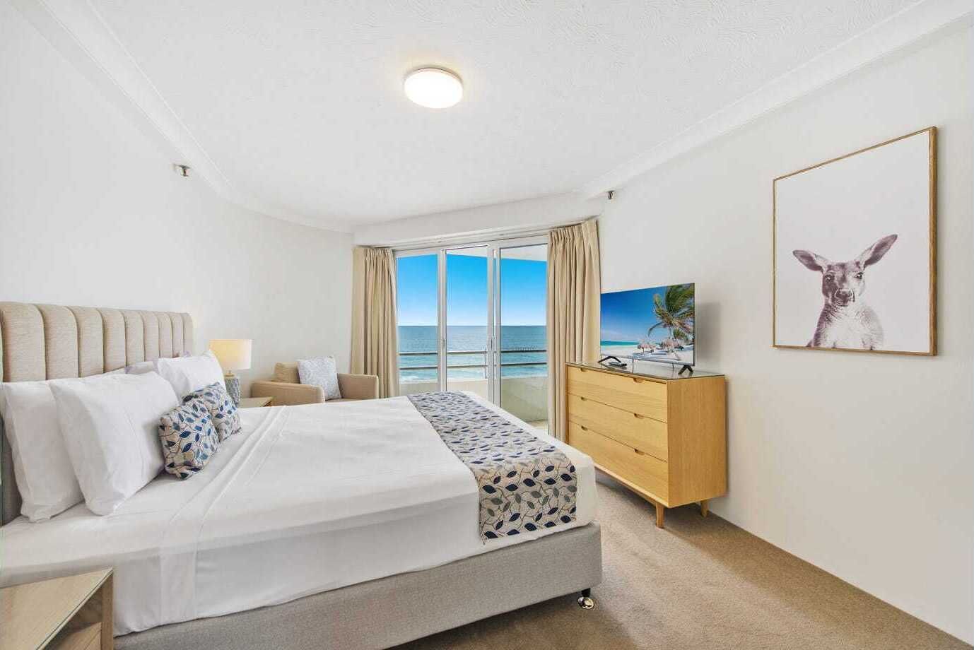 Ein Hotelzimmer mit Bett, Fernseher, Kommode und großem Fenster mit Meerblick.