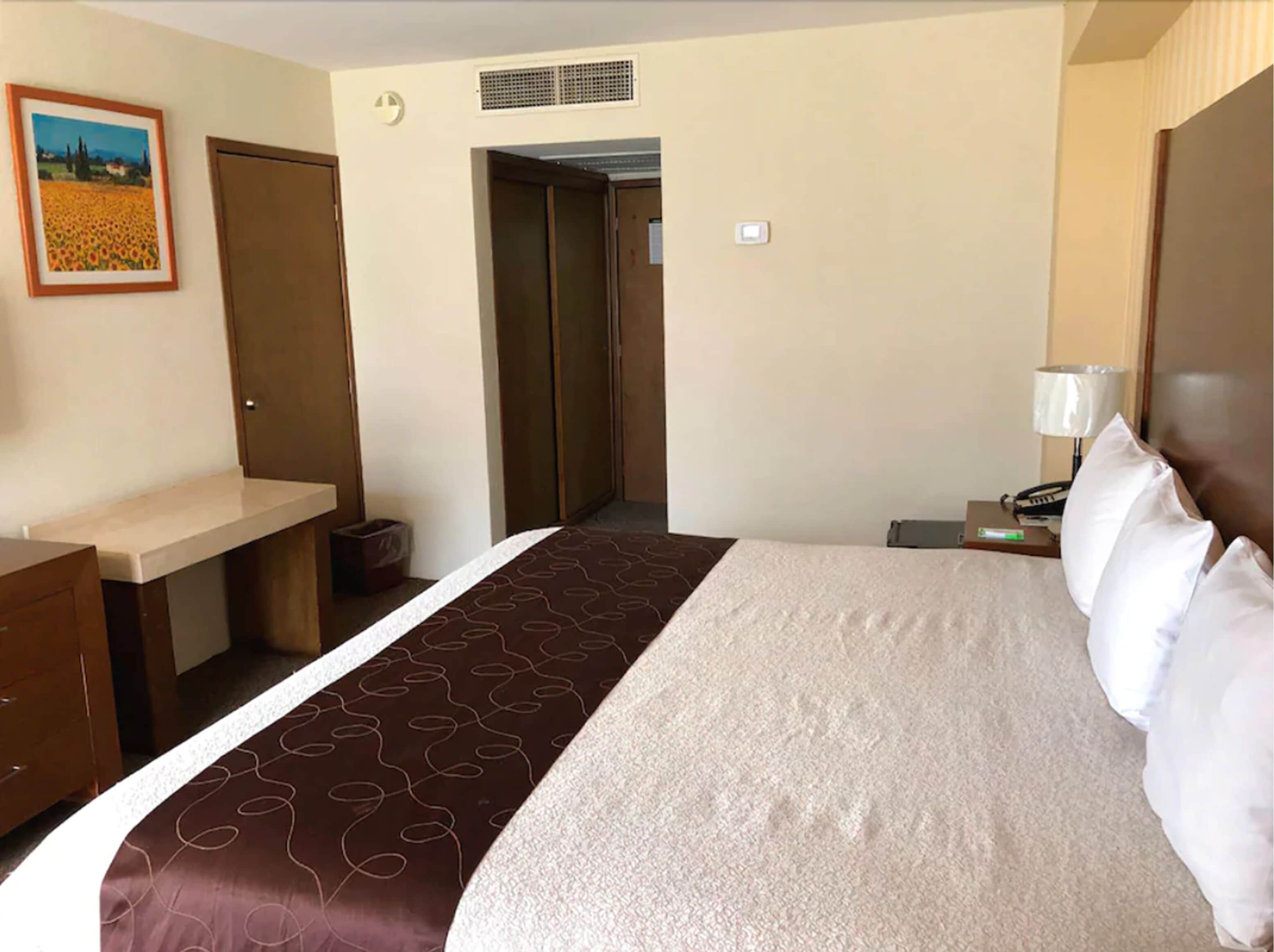 A hotel room with a bed, a desk, a chair, a lamp, and a picture on the wall.