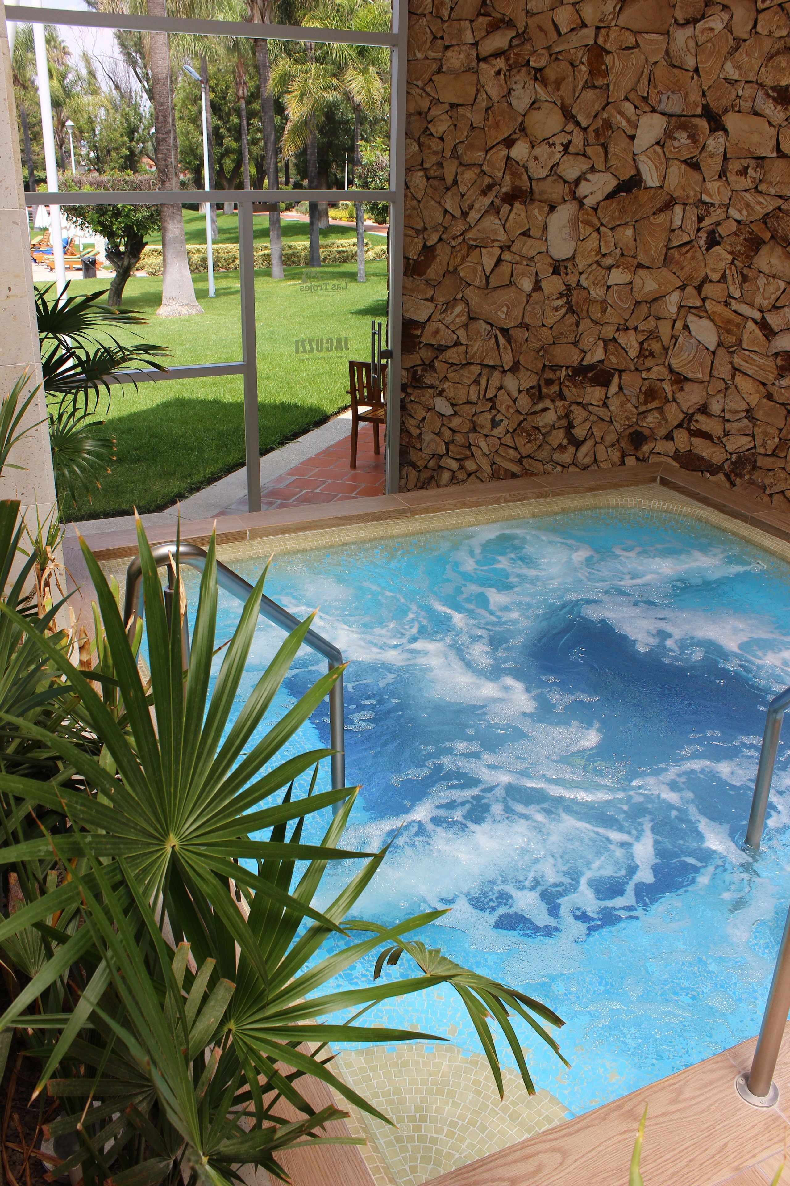 A hot tub with a stone wall and a view of a landscaped garden.