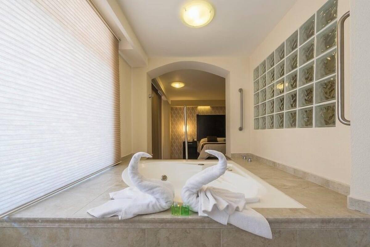 A bathroom with a bathtub, two swan-shaped towels, and a glass shower enclosure.