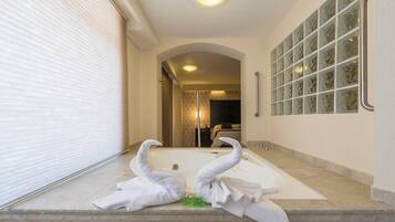 Un baño con una bañera, dos toallas con forma de cisne y un box de ducha de cristal.