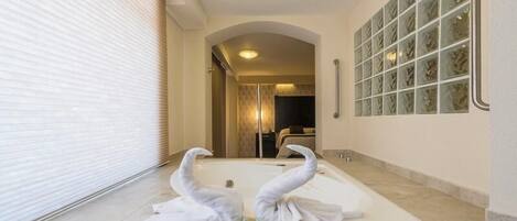 A bathroom with a bathtub, two swan-shaped towels, and a glass shower enclosure.