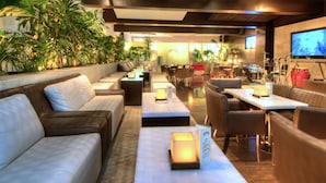 A modern lounge area with sofas, tables, and a stage with musical instruments. - Hotel Las Trojes (Aguascalientes)