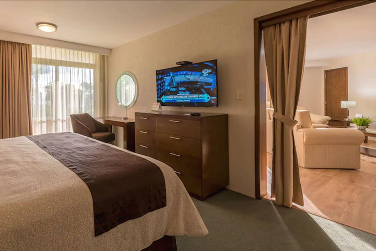 A hotel room with a bed, a desk, a television, and a seating area.