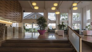 A spacious lobby with a wooden slatted wall, a large potted plant, and a staircase leading to upper floors. - Hotel Las Trojes (Aguascalientes)