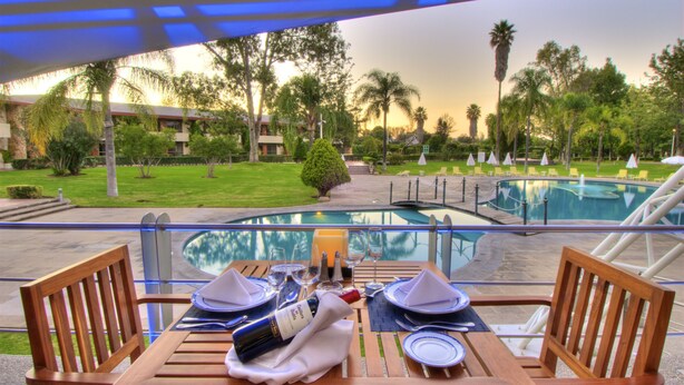 A dining table set for two with a view of a pool and palm trees. - Hotel Las Trojes (Aguascalientes)