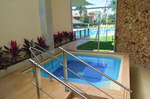 Una piscina con cubierta de madera y barandillas metálicas, rodeada de plantas y un muro de piedra.