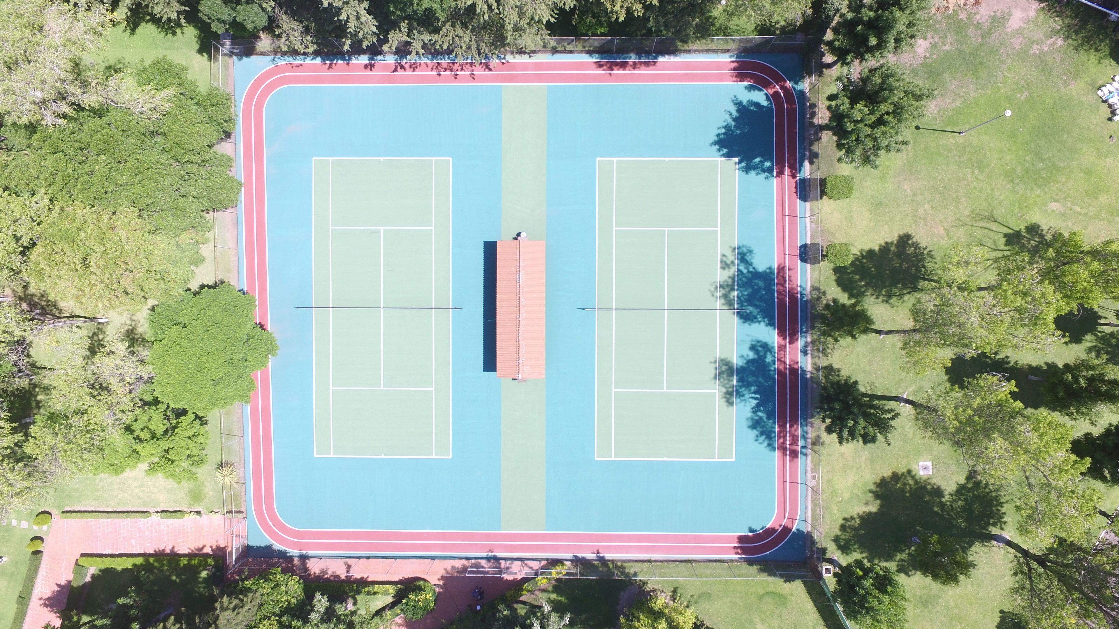 Vue aérienne d’un terrain de sport comprenant deux courts de tennis, entourés d’arbres et d’herbe.