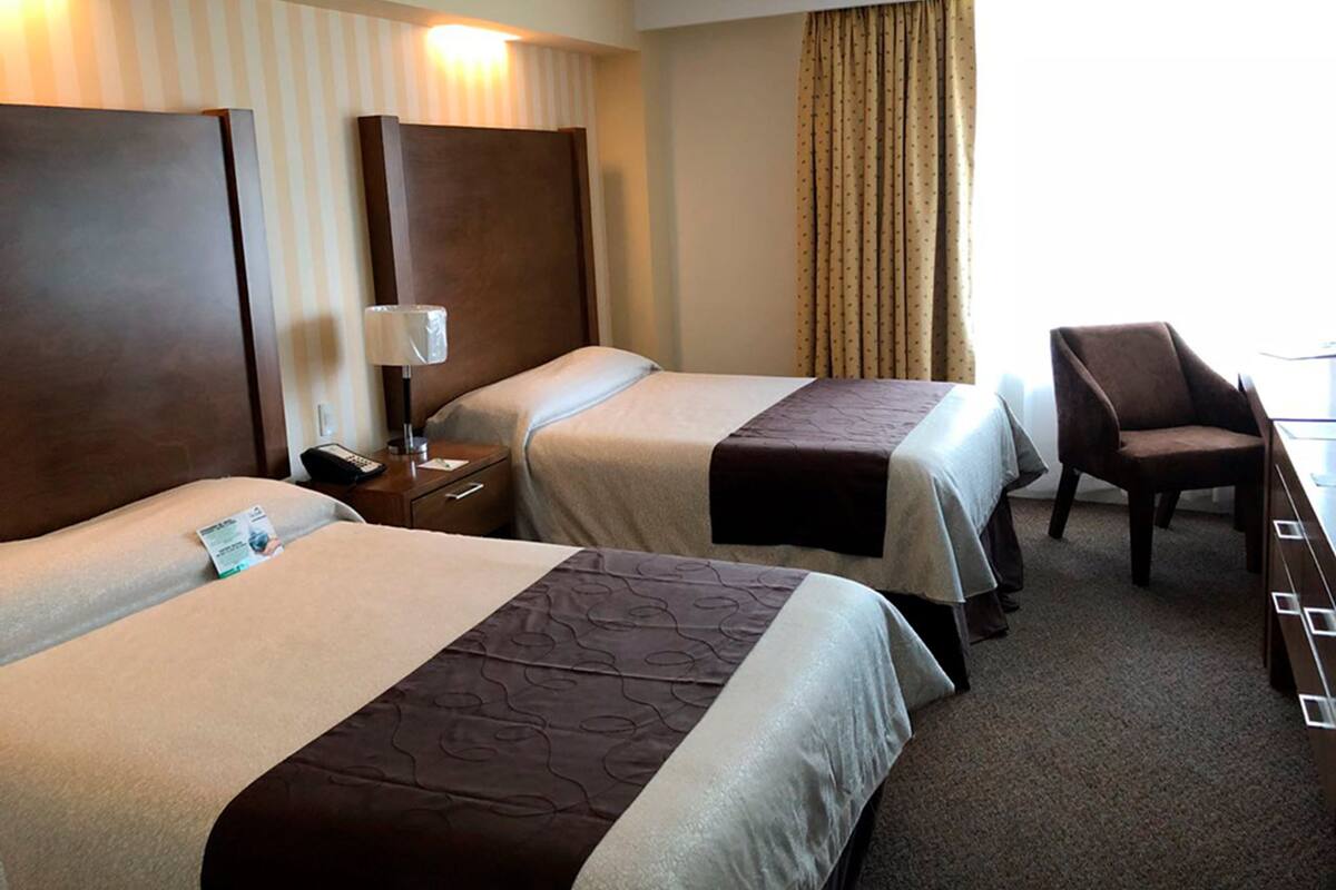 A hotel room with two beds, a desk, a chair, and a window with curtains.
