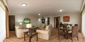 Una sala de estar moderna con un sofá, un sillón y una mesa de comedor con sillas. Hay un televisor montado en la pared y un cuadro sobre la mesa de comedor.
