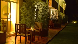 An outdoor seating area with wooden chairs and tables, surrounded by potted plants and a well-lit pathway. - Hotel Las Trojes (Aguascalientes)