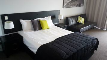 A hotel room with a large bed, a nightstand, a lamp, a chair, and a cityscape painting on the wall.