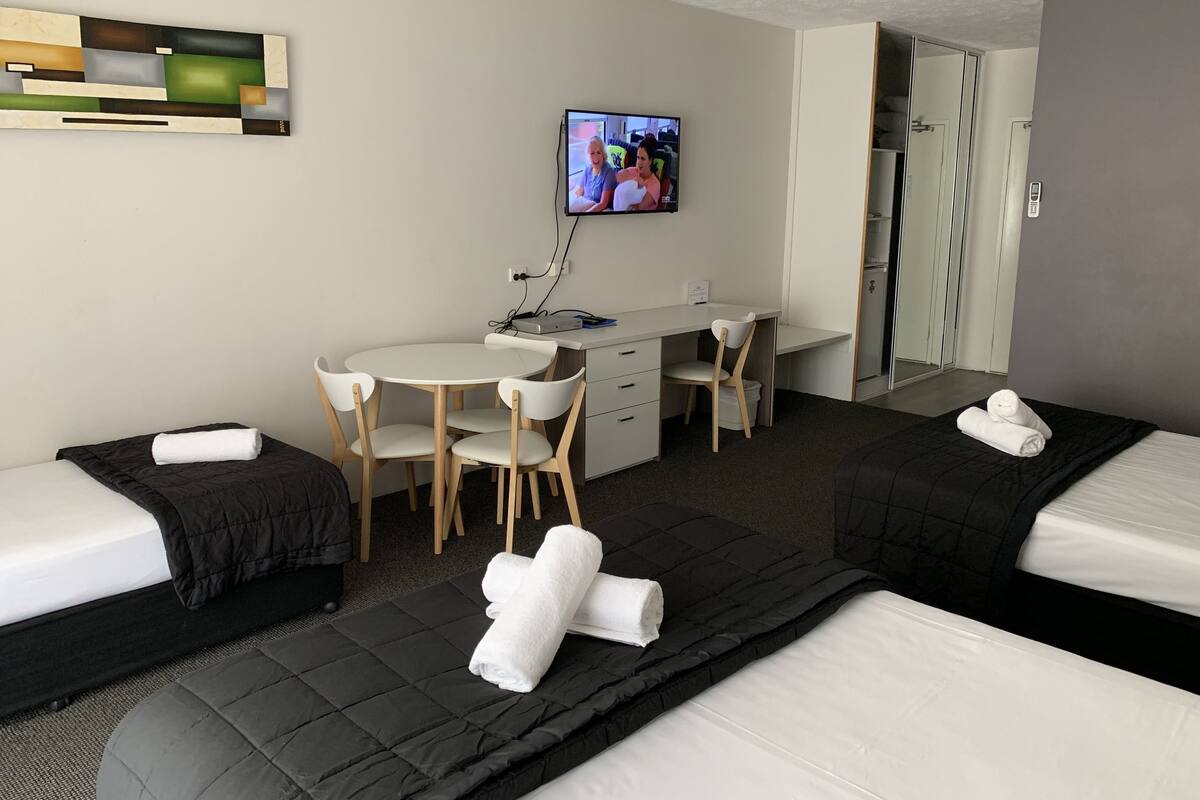 A hotel room with two beds, a desk, a chair, a television, and a bathroom visible through an open door.
