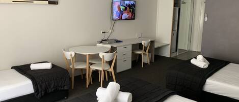 Camera d'albergo con due letti, una scrivania, una sedia, un televisore e un bagno visibile attraverso una porta aperta.