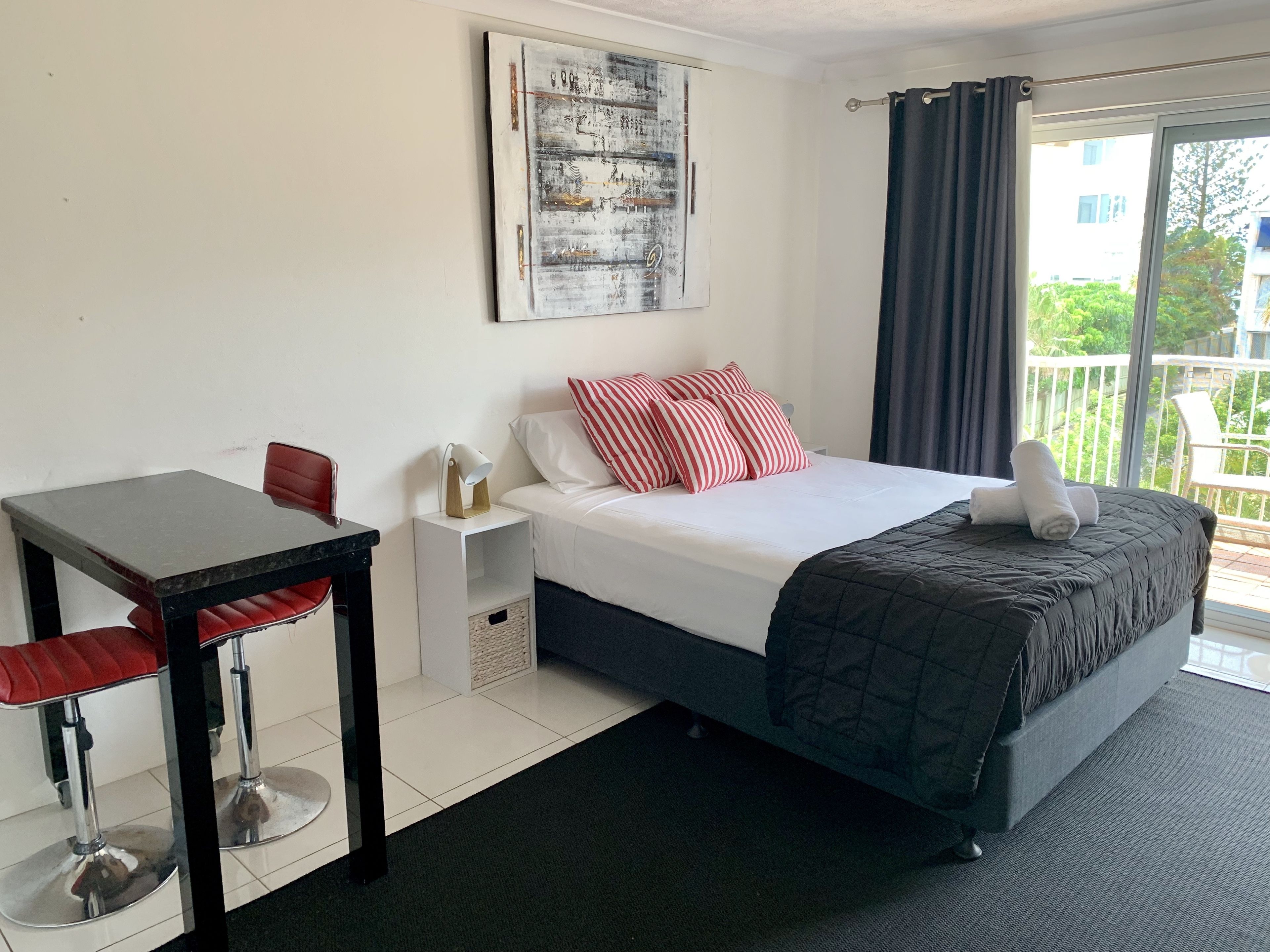 Een hotelkamer met een bed, een bureau, een stoel, een nachtkastje en een groot raam met gordijnen.