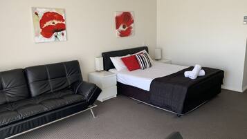 Habitación de hotel con un sofá de cuero negro, una cama con almohada a rayas negras y blancas, y dos cuadros de flores rojas en la pared.