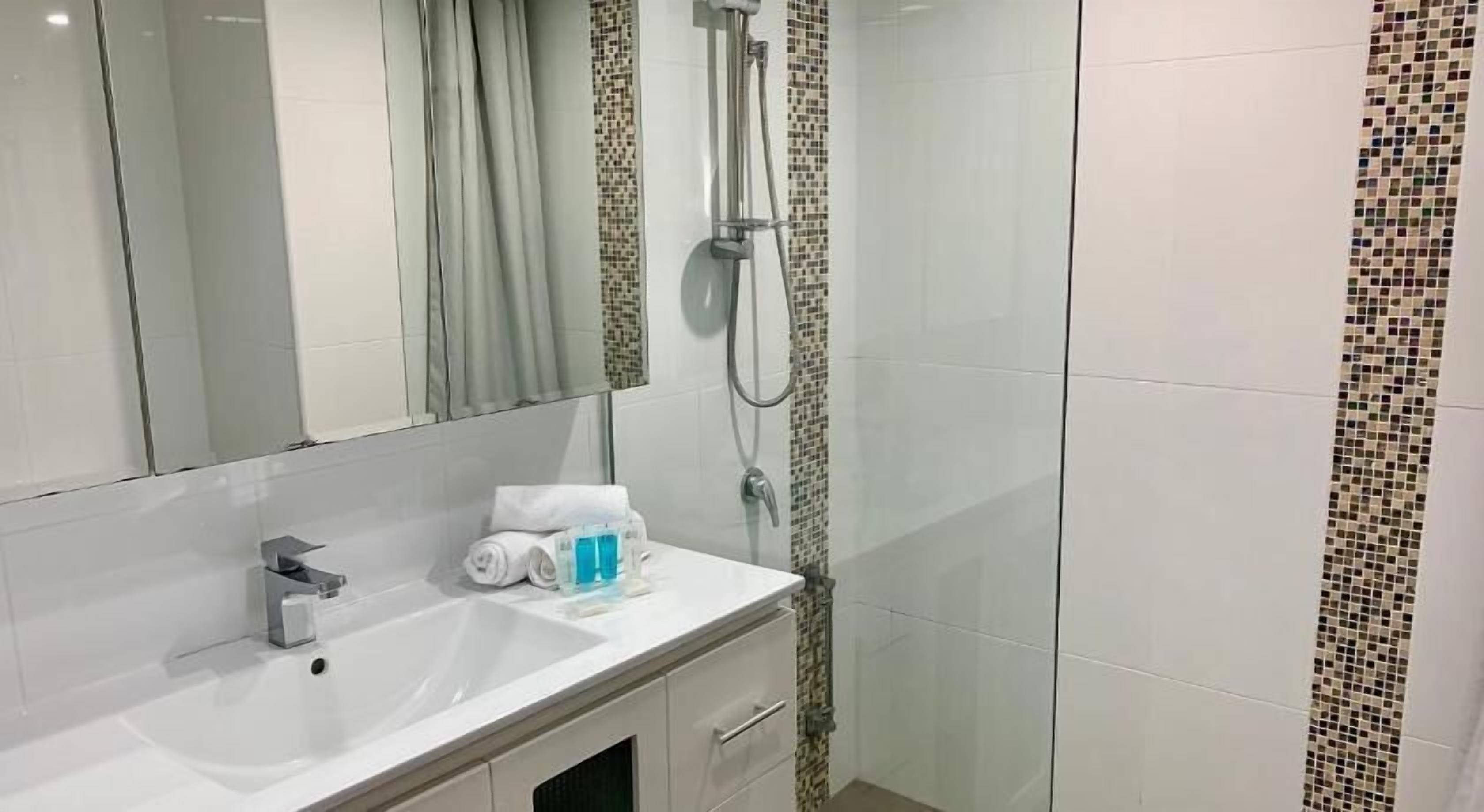 A bathroom with a sink, mirror, shower, and tiled walls.