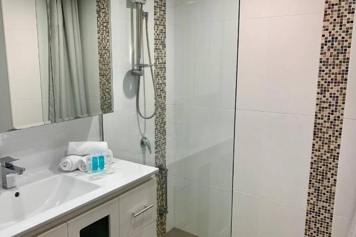 A bathroom with a sink, mirror, shower, and tiled walls.