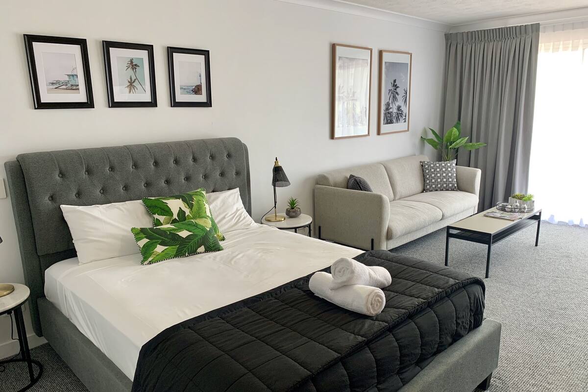 A hotel room with a bed, a sofa, a coffee table, and a plant.