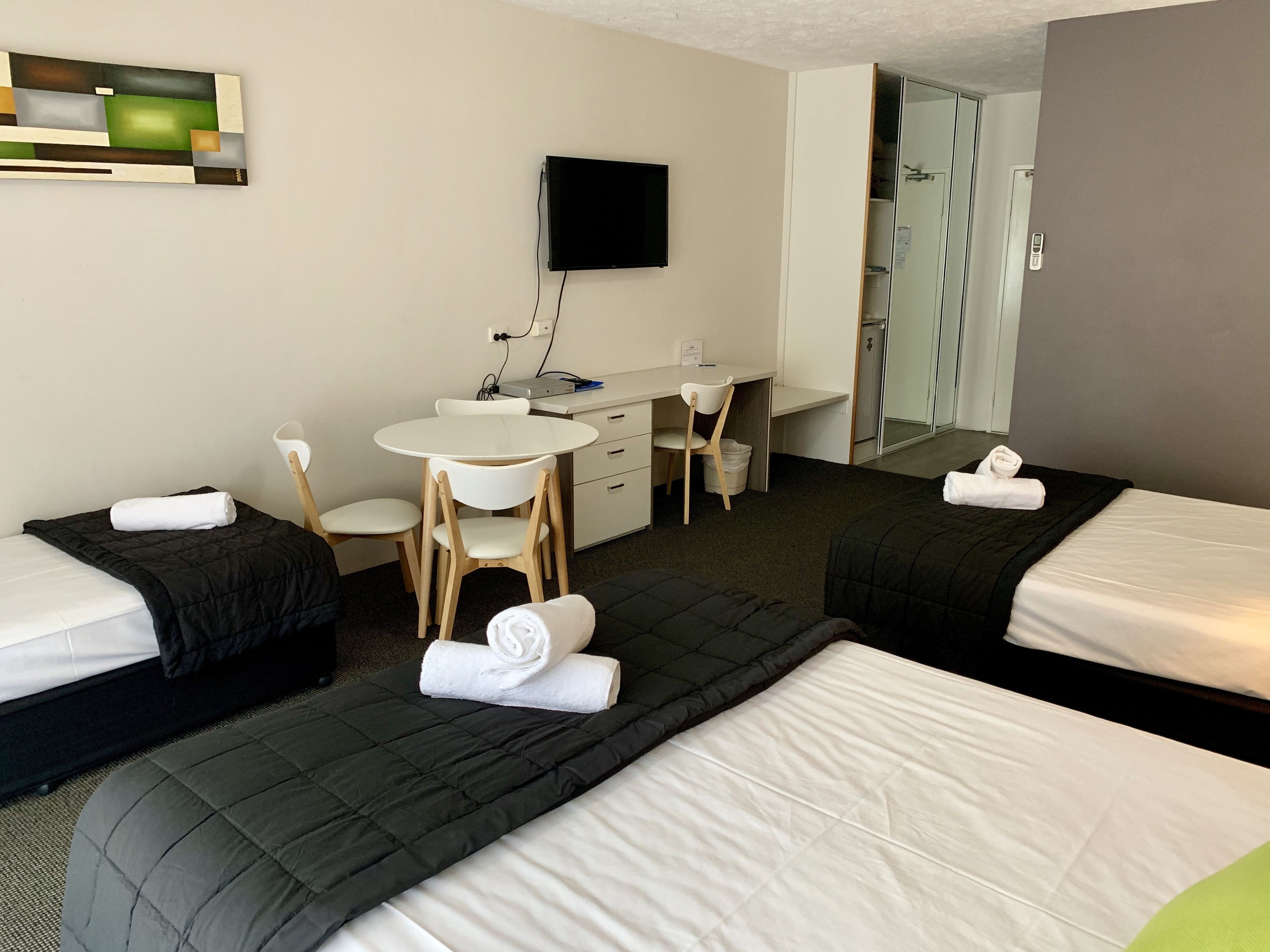 A hotel room with two beds, a desk, a chair, a television, and a bathroom visible through an open door.