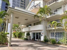 Un hotel de varios pisos con entrada techada, palmeras y un paseo de ladrillo.