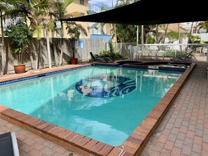 Relax by the pool surrounded by lush greenery and a wooden fence.