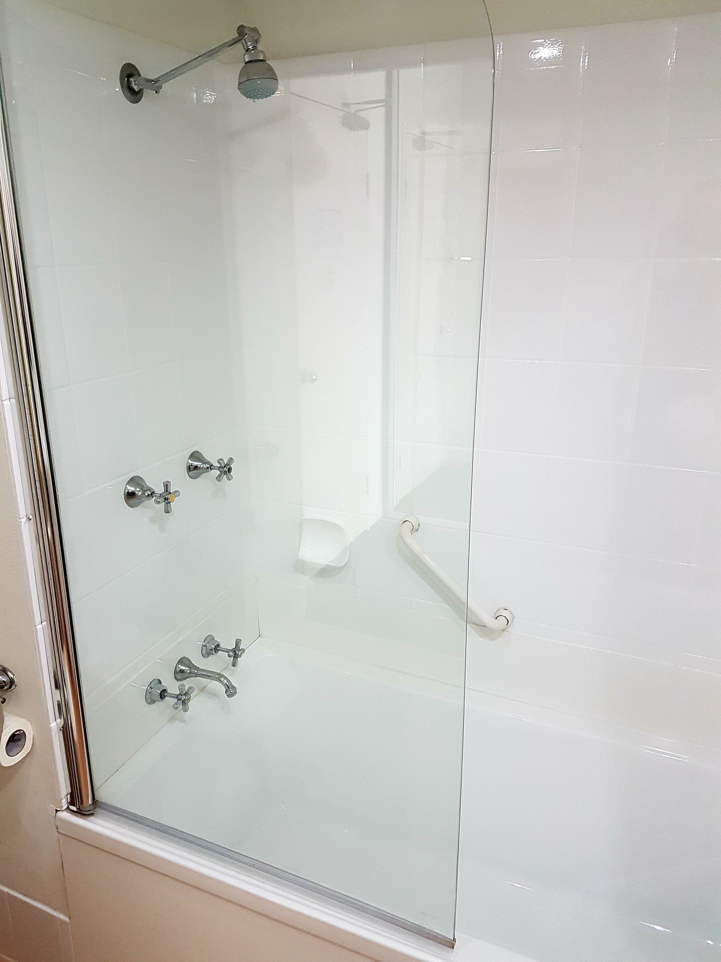 A glass-enclosed shower with a handheld showerhead and a handheld faucet.