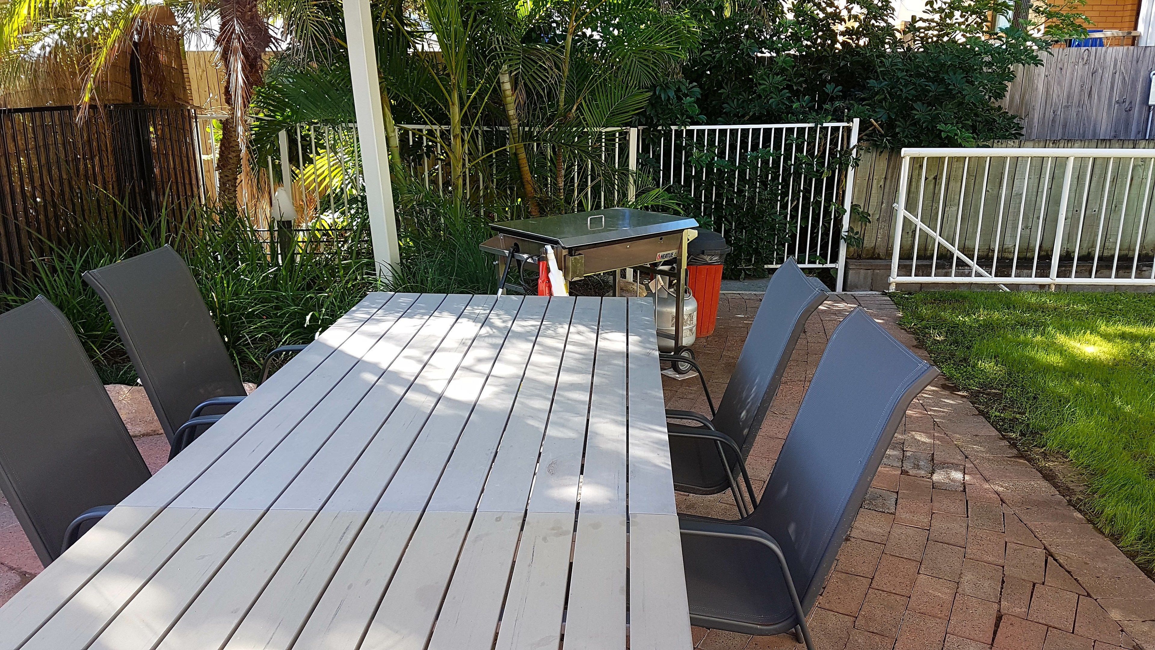 A patio with a table and chairs, surrounded by a wooden fence and greenery.