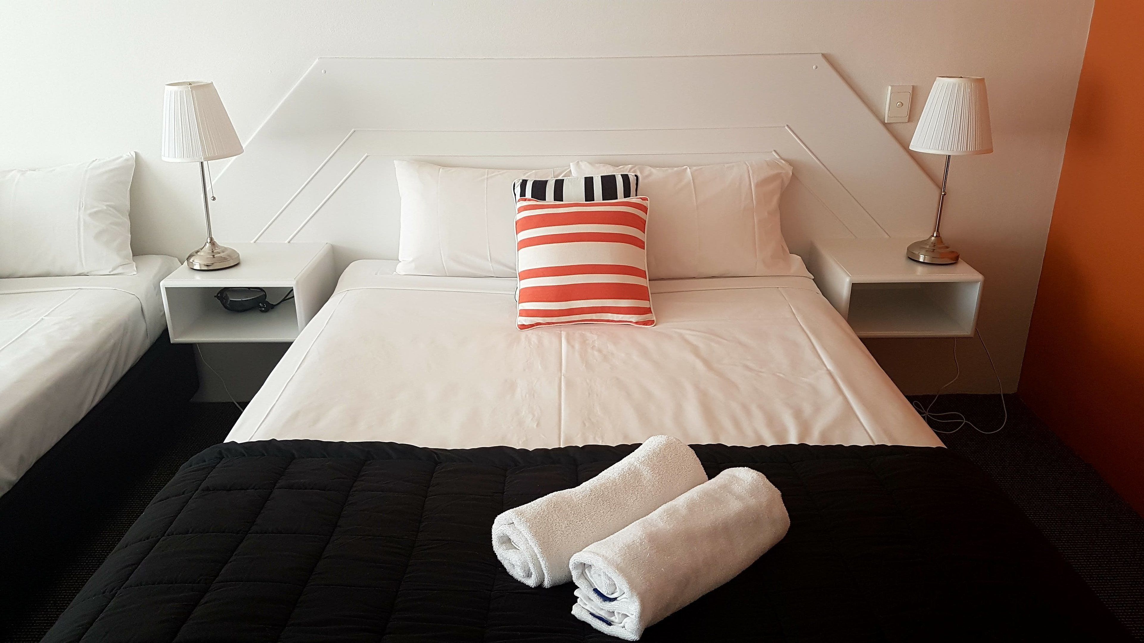 Une chambre d’hôtel comprenant un lit, deux lampes de chevet, un oreiller, une table de chevet et une couvre-lit noire matelassée.