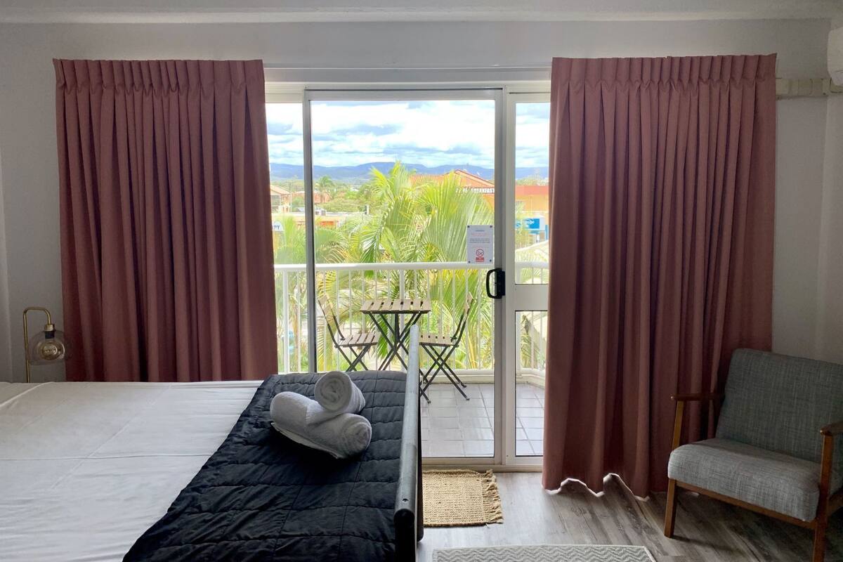 A hotel room with a bed, a chair, a small table, and a balcony with curtains.