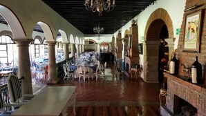 Un restaurante espacioso con techos altos, columnas arqueadas y una chimenea de ladrillo. Las mesas y sillas están dispuestas para comer.