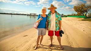A couple standing on a sandy beach with a body of water and a bridge in the background. - Broadwater Tourist Park (Southport)