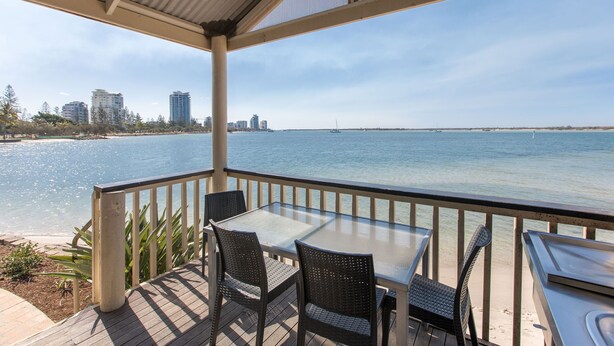A covered outdoor area with a table and chairs, overlooking a beach and the ocean. - Broadwater Tourist Park (Southport)