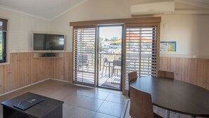 A room with a television, a table, and a chair. There is a sliding door leading to an outdoor area with a table and chairs. - Broadwater Tourist Park (Southport)