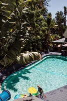 Una piscina rodeada de exuberante vegetación, con una terraza de madera y un área de estar cubierta.