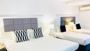 A hotel room with two beds, each with a headboard, white bedding, and black and white patterned pillows. There are bedside tables with lamps. - Greenmount Beach House (Coolangatta)