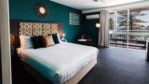 A hotel room with a large bed, a ceiling fan, a view of the outdoors, and a seating area with a table and chairs. - Greenmount Beach House (Coolangatta)