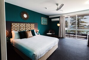 Habitación de hotel con una cama grande, ventilador de techo, vistas al exterior y una zona de estar con mesa y sillas.