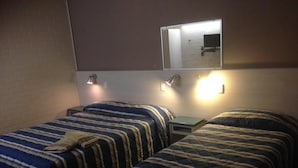 Una habitación con dos camas, cada una con ropa de cama a rayas, una mesita y un espejo colgado en la pared.