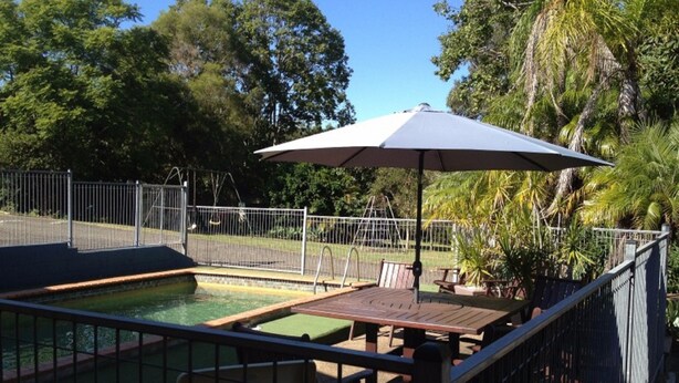 Una piscina con un borde cercado, una mesa, sillas y una sombrilla.