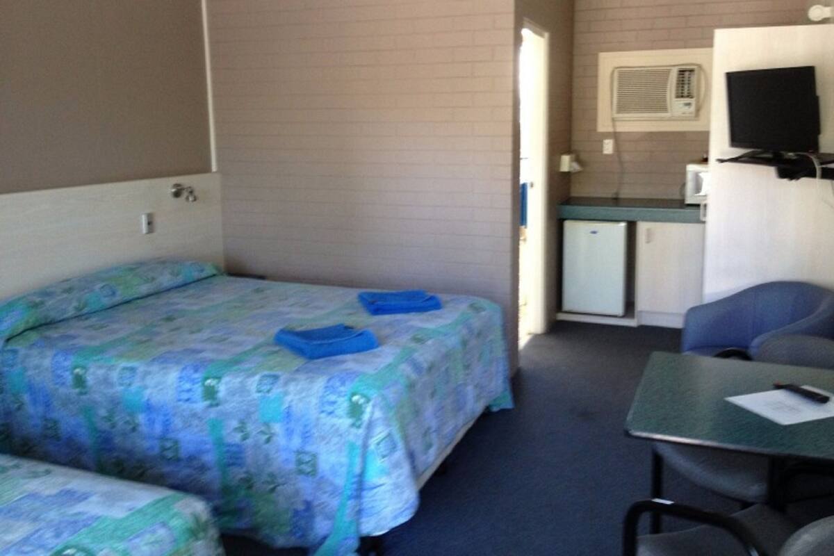 A room with two beds, a small kitchenette, a television, and a table with a chair.