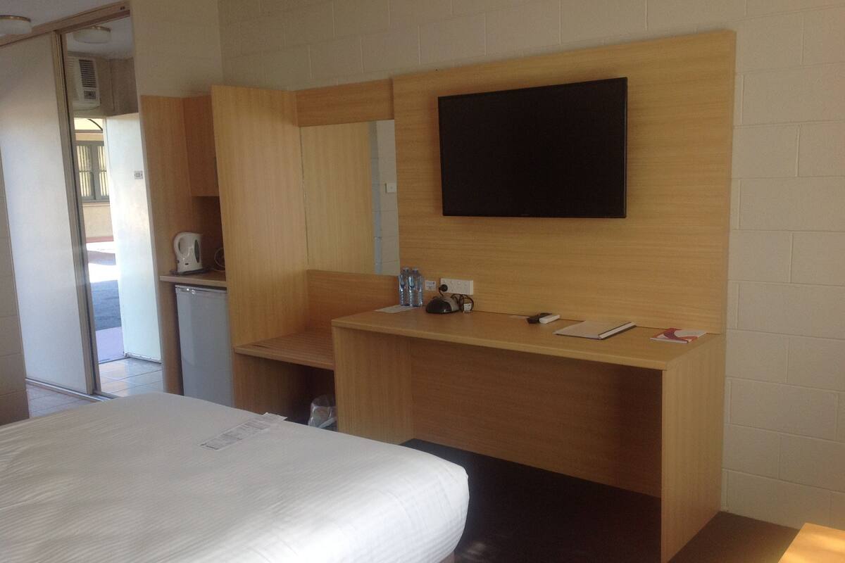 A hotel room with a bed, a wooden desk, a flat-screen TV, and a small kitchenette.