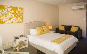 A hotel room with a bed, a sofa, a bedside table with a lamp, a phone, and a painting on the wall.