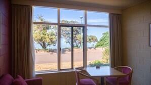 A room with a large window, a table, two chairs, and a purple sofa. - Foreshore Motor Inn (Whyalla)
